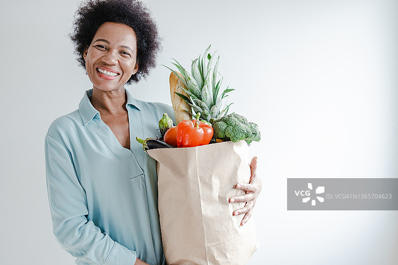 在白墙前手提杂货袋的非洲裔女子肖像图片素材