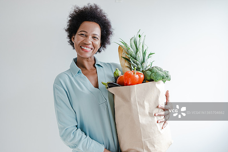 在白墙前手提杂货袋的非洲裔女子肖像图片素材