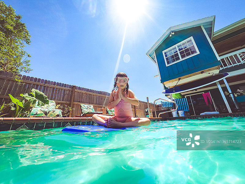 可爱顽皮的女孩戴着游泳镜在家庭住宅后院的游泳池里玩耍图片素材