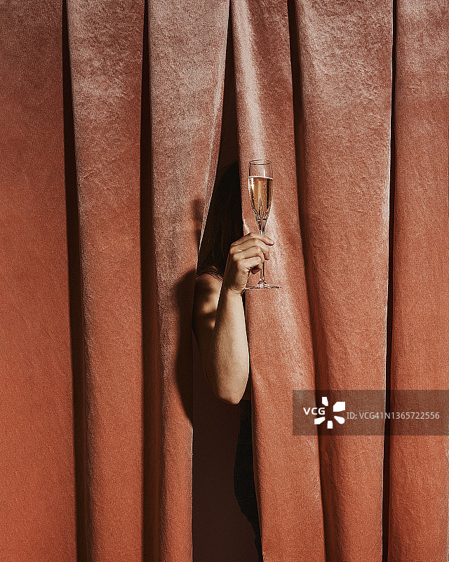 一位女士站在天鹅绒幕布后举杯香槟庆祝图片素材