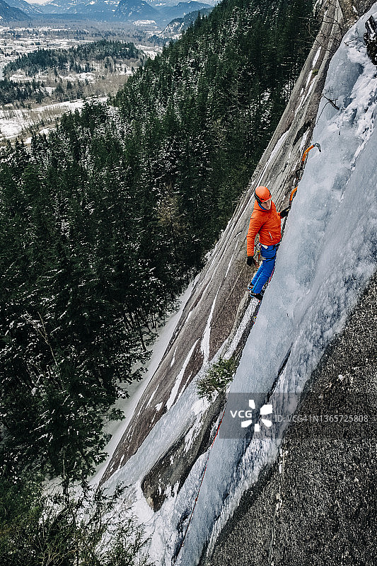 不列颠哥伦比亚省，一名男性攀冰者单手握冰镐在高空攀爬图片素材