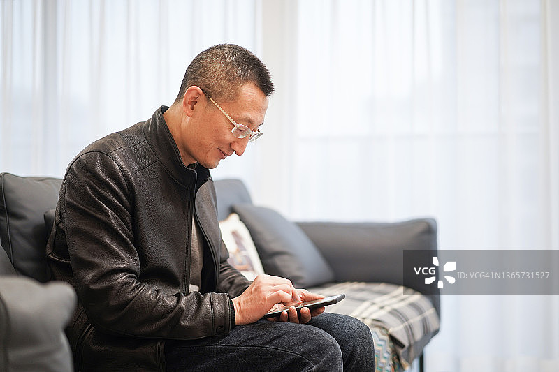 男人坐在沙发上在客厅里使用手机图片素材