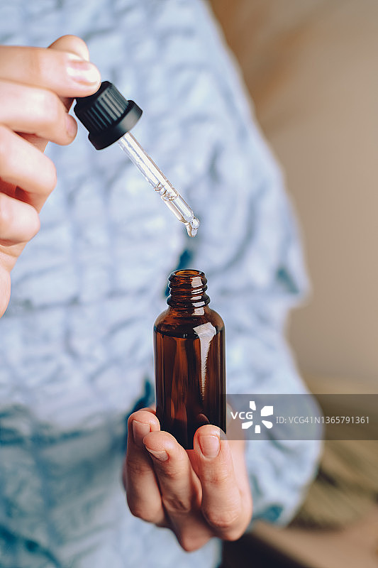 女人手持滴管瓶，内含维生素C抗衰老面部护肤精华液或去角质产品图片素材