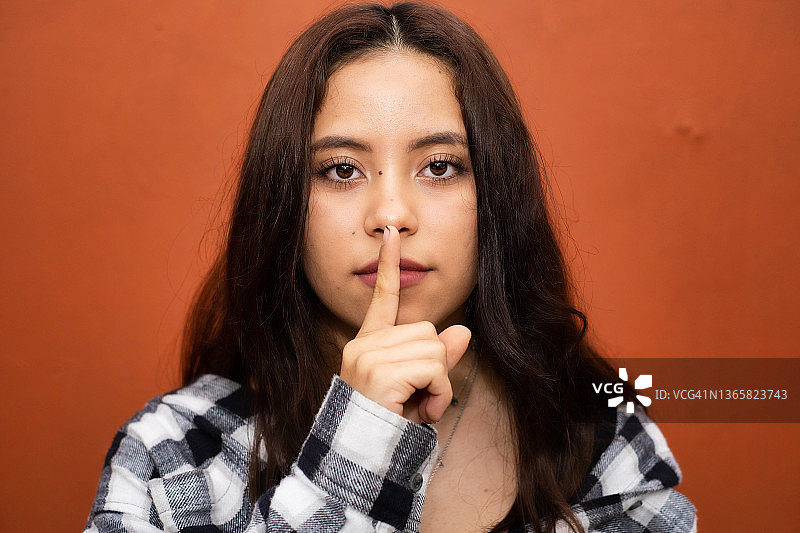 年轻的拉丁裔女人看着镜头，手指放在嘴唇上，示意安静图片素材