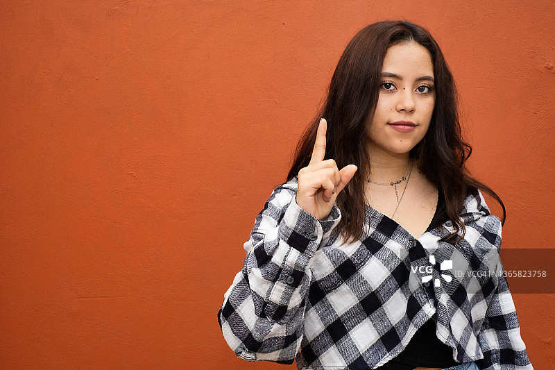 年轻的拉丁裔女人微笑，看着镜头并做出“第一”的手势图片素材