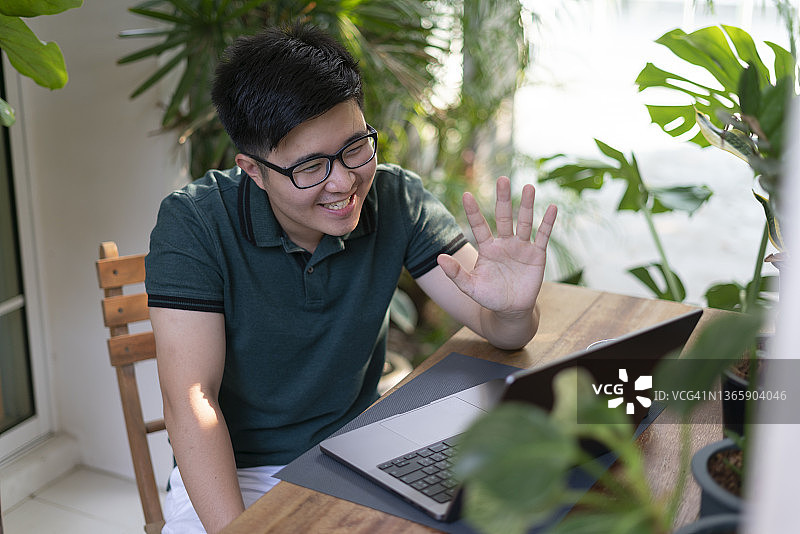年轻男子在家中与朋友进行视频通话的照片。多人通过笔记本电脑进行在线会议。隔离期间朋友们进行在线交谈。图片素材