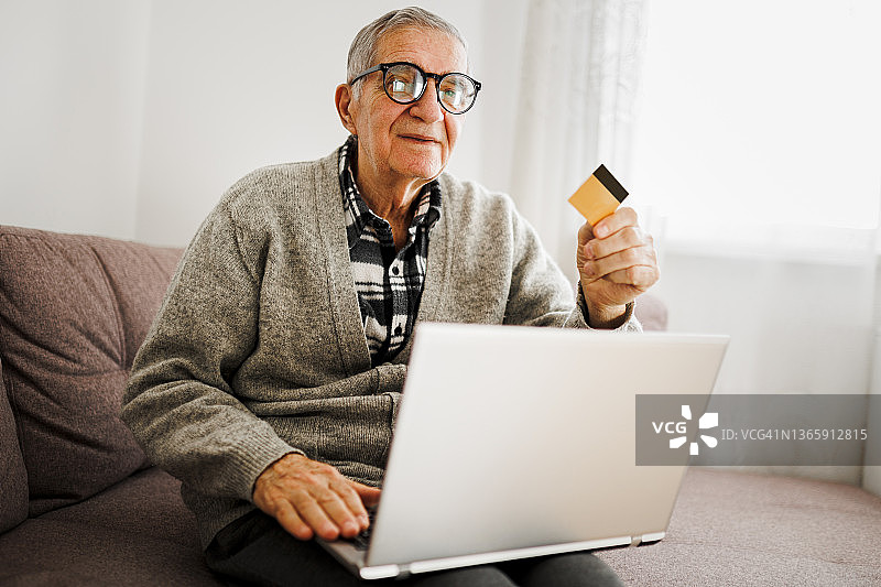 坐在沙发上用笔记本电脑和信用卡的年长男人图片素材