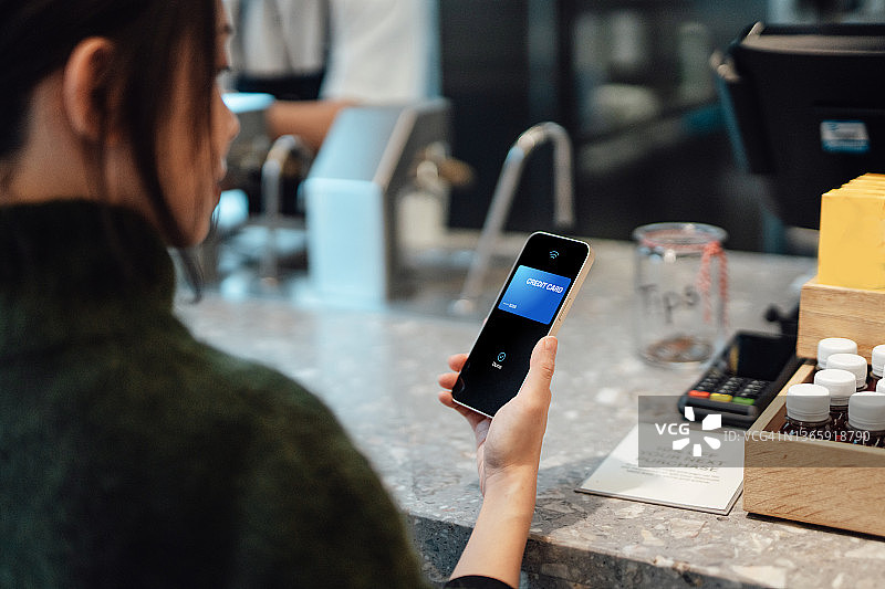年轻女子在咖啡馆用智能手机进行移动支付点咖啡的特写镜头图片素材