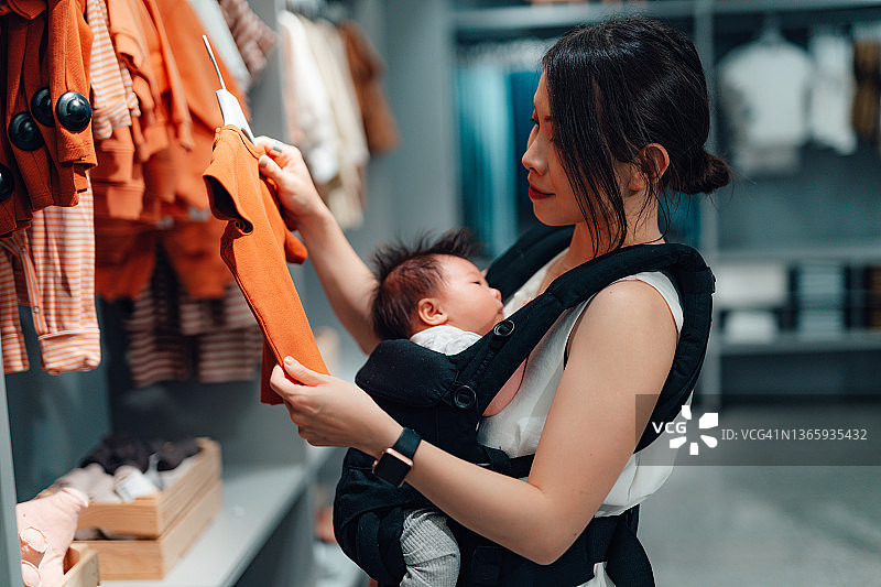 年轻的亚裔母亲在商场为宝宝购买服装图片素材