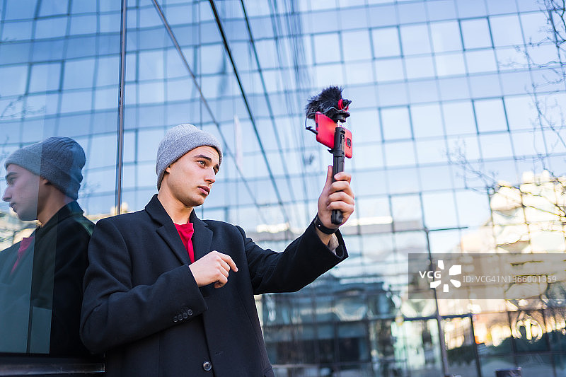 年轻微笑的家伙用他的红色手机和麦克风录制视频博客，在互联网上与他的追随者进行社交网络交谈图片素材