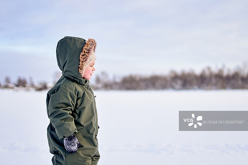 穿着绿色冬季连体衣的3岁男孩在雪地里行走图片素材