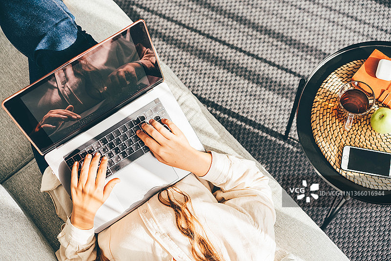在家中沙发上使用电脑线上工作的卷发自由职业女性图片素材