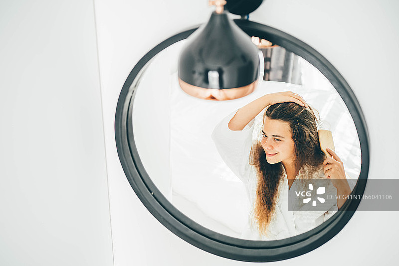 穿着浴袍的年轻女子，对着圆镜微笑，梳理着长长的卷发图片素材