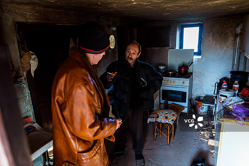 简陋的家中，两位年长的男人一边抽烟一边交谈图片素材