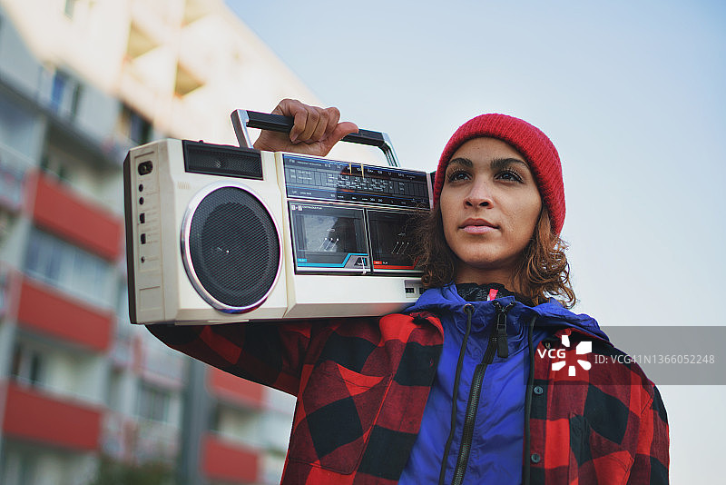 低角度拍摄：在城市户外，携带立体声收音机听音乐的年轻女性图片素材