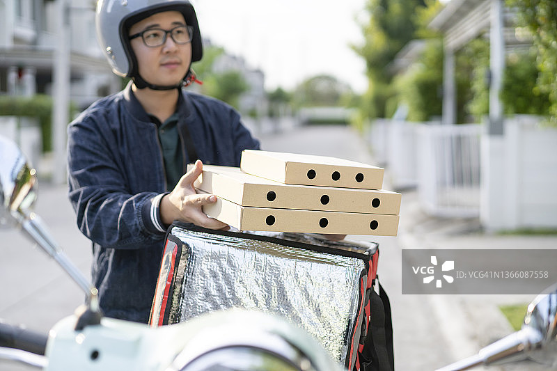 手拿快递盒的年轻亚洲男人，摩托车配送食品特快服务概念图片素材