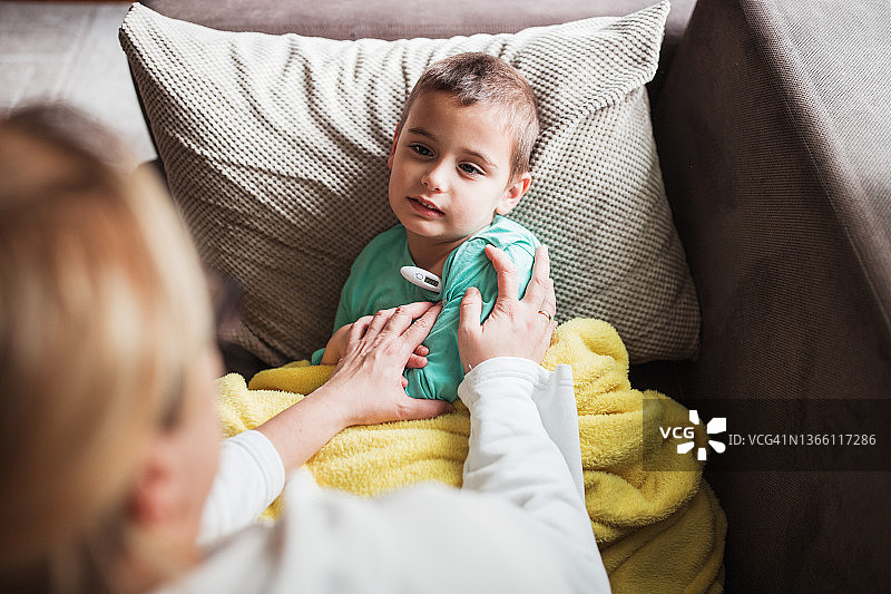 生病的男孩胳膊下夹着温度计看着他的妈妈图片素材
