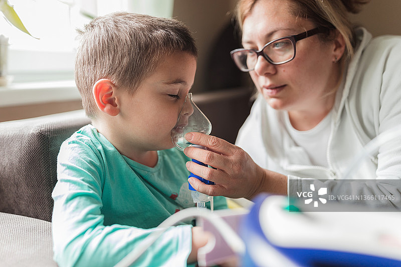 年轻妈妈用雾化器为生病的儿子做雾化图片素材