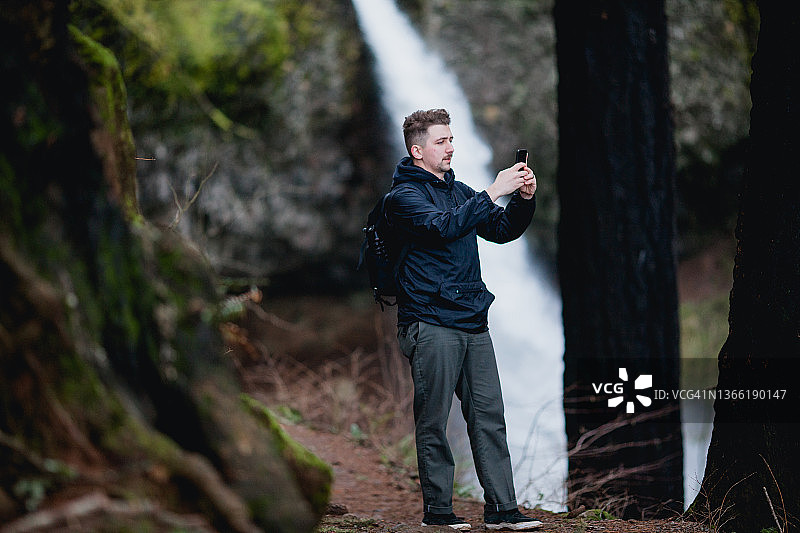 徒步旅行者在瀑布附近用智能手机拍照图片素材