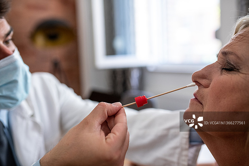 特写：医生为年长的金发女人进行鼻拭子新冠检测采样图片素材