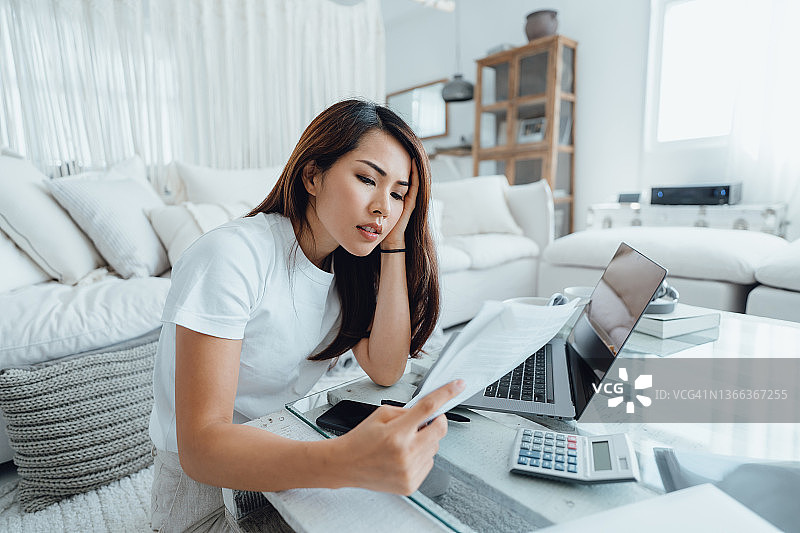 用笔记本电脑处理家庭财务的年轻亚洲女性，查看账单时显得很担忧。财务计划、税务、支出和预算、财务问题概念图片素材