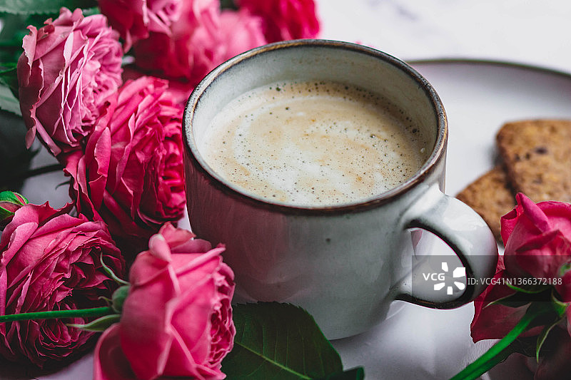 玫瑰花簇拥的牛奶咖啡杯，女士的早安礼物图片素材