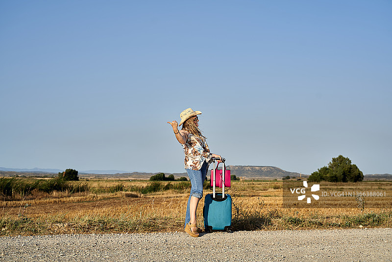 在泥泞的道路上搭便车的、拿着行李箱的年轻女人图片素材