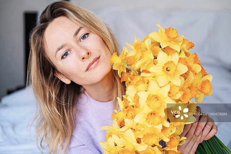 特写：手捧一束春天黄色鲜花的年轻漂亮金发女孩图片素材