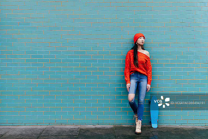 年轻的亚洲女性靠在瓷砖墙上，手拿滑板图片素材