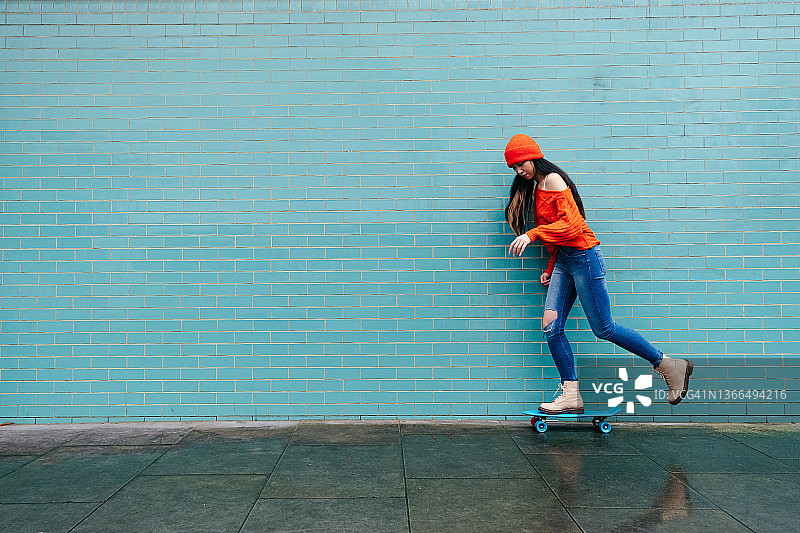 靠在砖墙上滑冰的时尚年轻女人图片素材