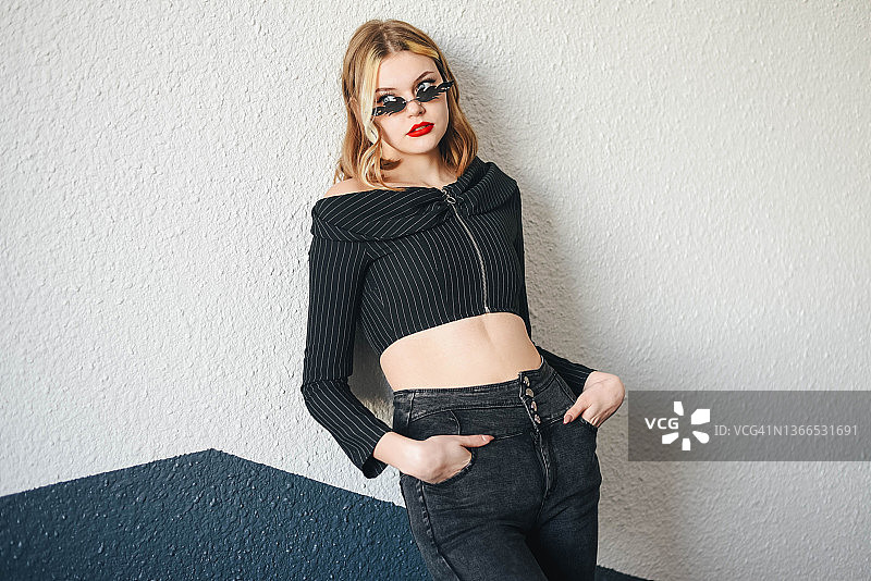 戴眼镜的金发女孩靠墙站立图片素材