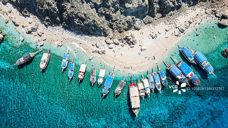 孤岛航拍：碧绿海水中的波浪与沙滩，岛屿背景，停靠在岛上的船只，人们在碧绿海水中游泳，在海滩岛屿上游泳和日光浴图片素材