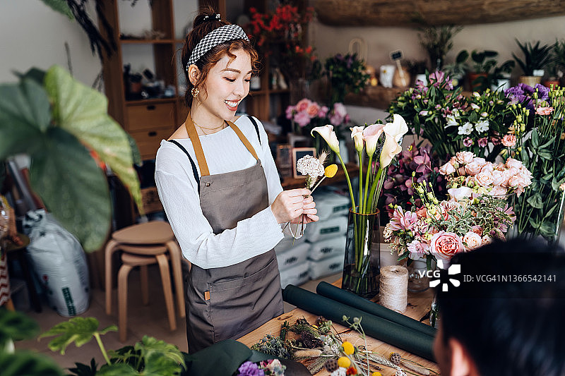 亚洲青年女花艺师，小花店店主，举办插花工作坊，向学生讲授花束制作课程。图片素材
