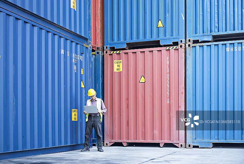 一位年长的工人在造船厂使用笔记本电脑检查货运集装箱图片素材