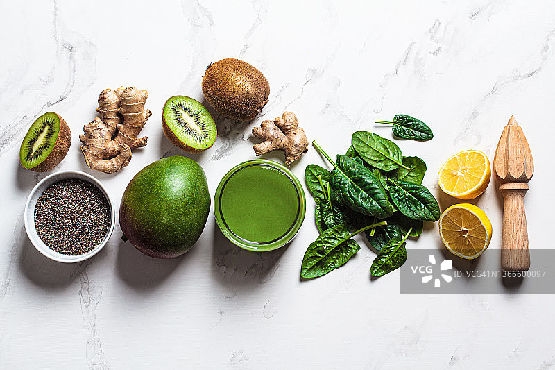 白色大理石背景上的绿色菠菜芒果冰沙与配料，排毒饮品概念图片素材