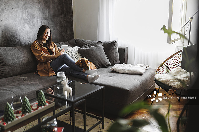 笑容满面的女人和她的狗一起休息，并在平板电脑上看杂志图片素材