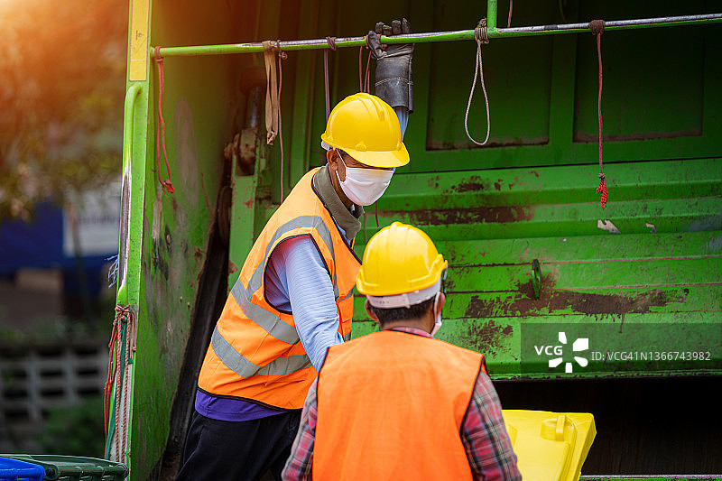 在城市工作的垃圾工人，两名工人在垃圾收集车上装载混合生活垃圾图片素材