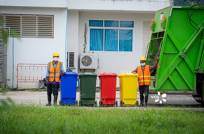 在城市工作的垃圾工人，两名工人在垃圾收集车上装载混合生活垃圾图片素材