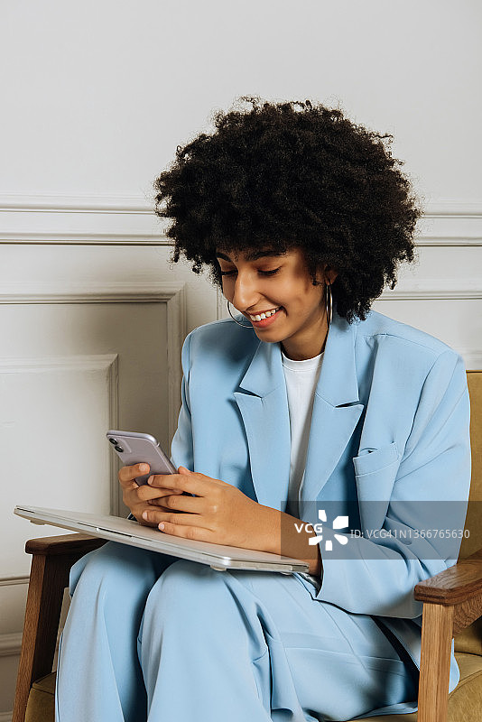 一位快乐的非裔美国女性坐在椅子上，通过智能手机在线聊天图片素材