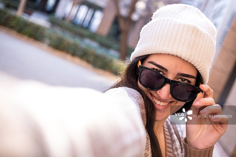 一个年轻的女孩戴着墨镜在城市里自拍图片素材