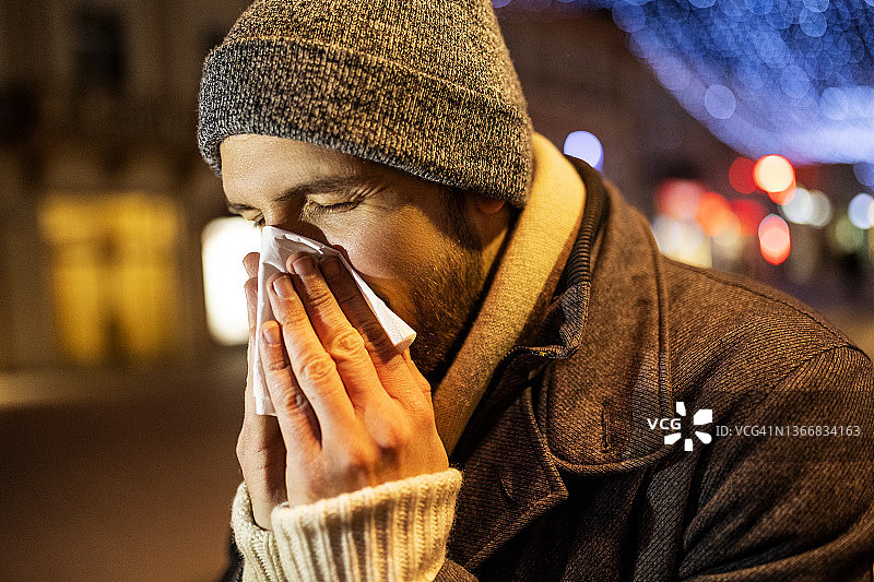 在街上擤鼻子的患感冒或流感的年轻男人图片素材