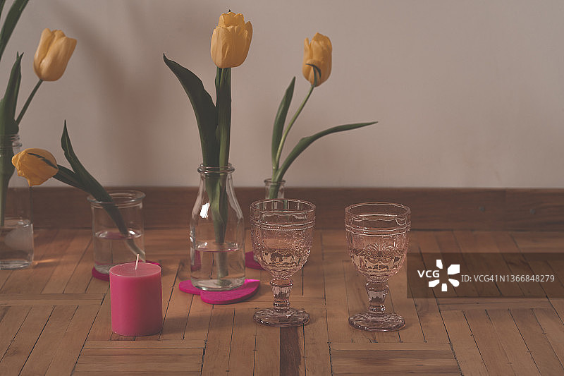 饮品，花瓶中的黄色郁金香，粉色葡萄酒杯，再生木地板上的粉色蜡烛图片素材