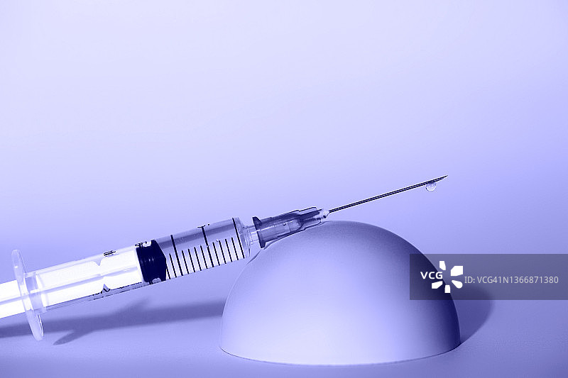 紫色背景上半圆形台上的药液注射器特写图片素材
