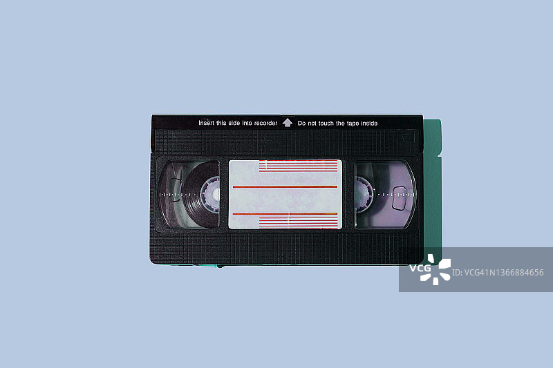 蓝色背景上的黑色VHS录像带，具有硬阴影。视频、电影、复古、怀旧、过时、磁性和电影系统概念图片素材