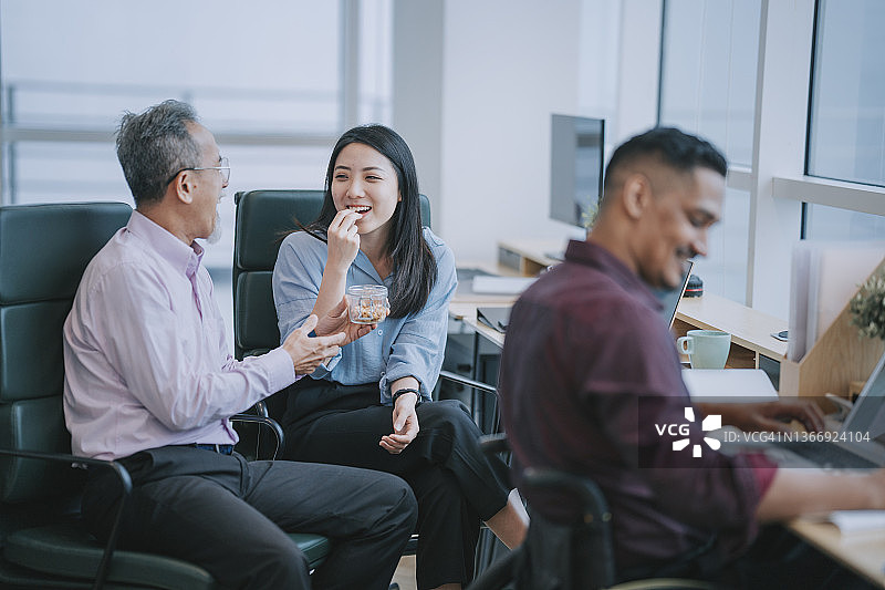 亚洲白领在工作站办公室一起休息吃零食图片素材