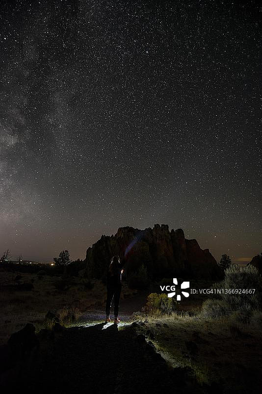 年轻女子在峡谷小路上用手电筒照亮夜空图片素材