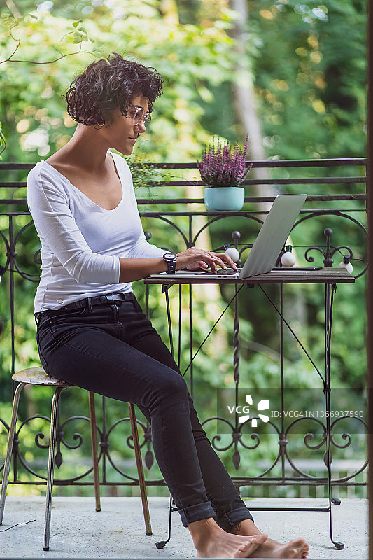 年轻女子坐在阳台上用笔记本电脑在家工作图片素材