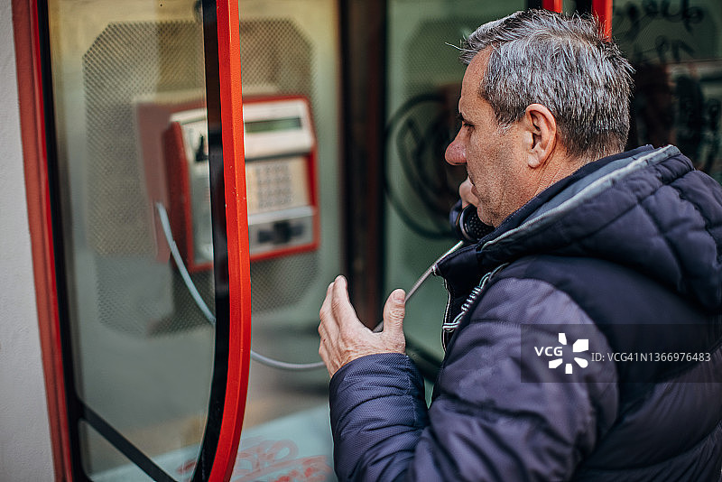 一位中年男子在城市街道上使用电话亭图片素材