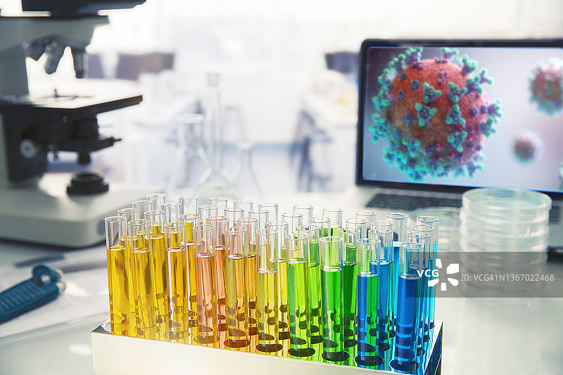 实验室桌子上紧挨着屏幕上冠状病毒的彩色小瓶图片素材