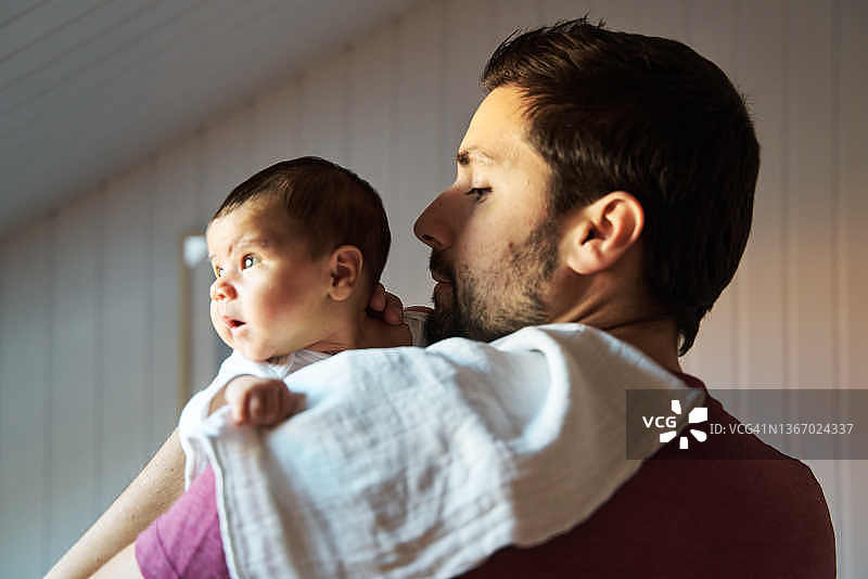父亲肩上披着毯子，充满爱意地抱着新生女婴的背影图片素材